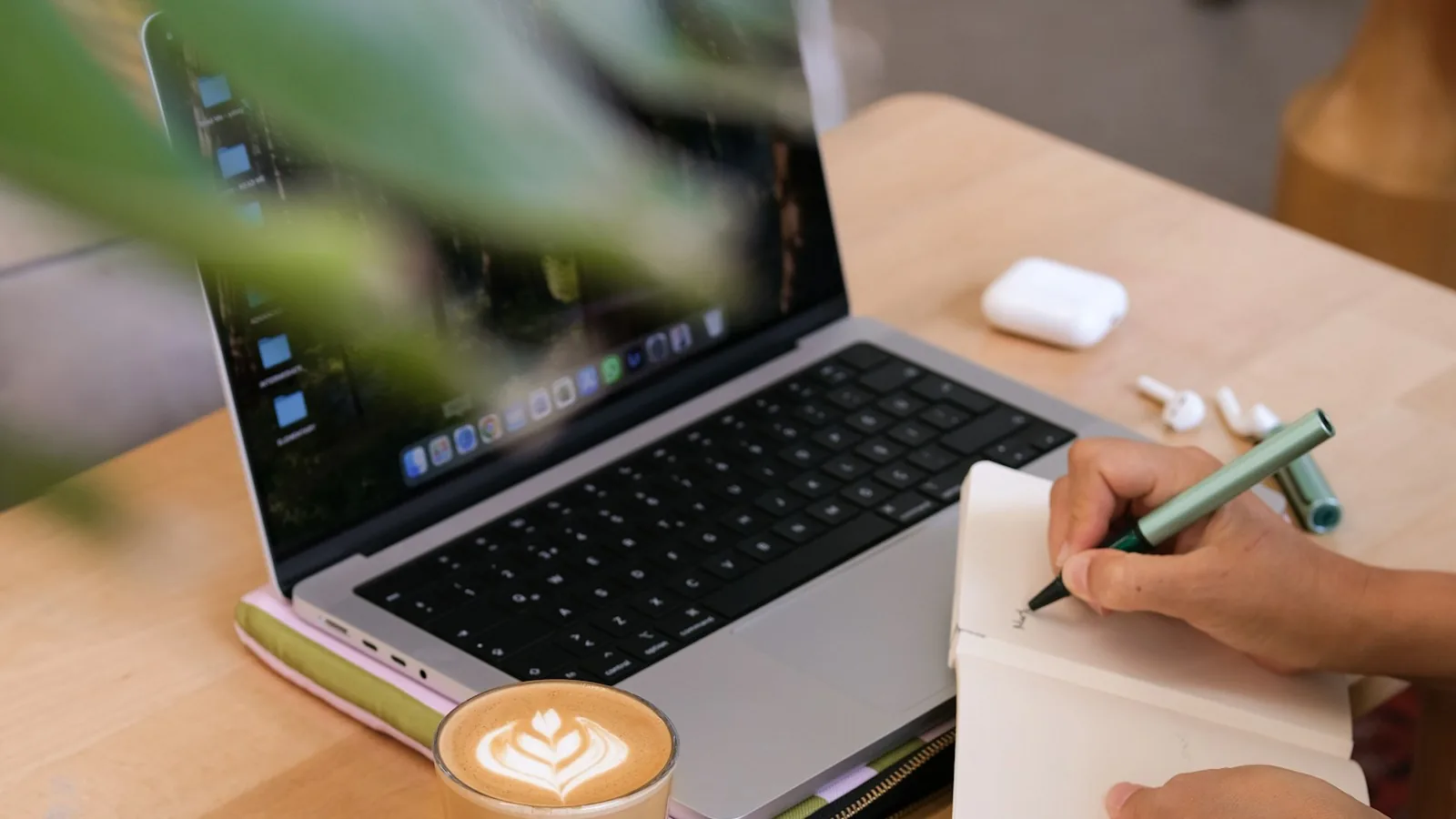 Person handwriting notes in a notebook next to a MacBook and latte, illustrating a private on-device note-taking workflow