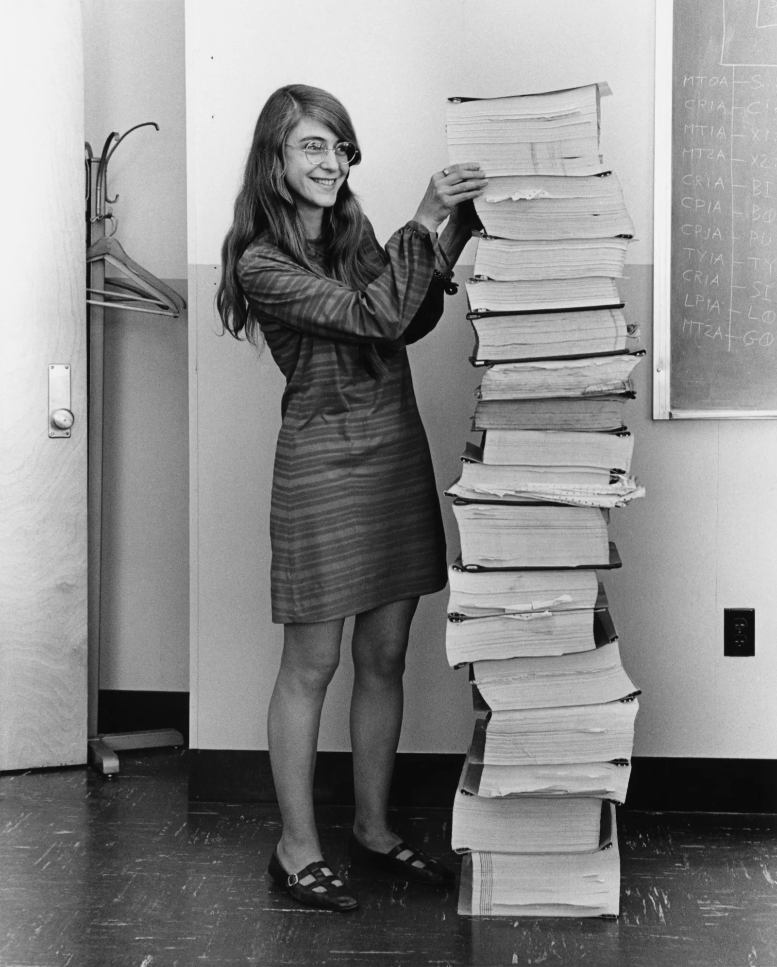 Margaret Hamilton standing beside a tall stack of program listings from the Apollo Guidance Computer software